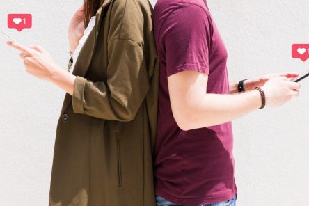 couple-standing-back-back-using-cellphone-with-love-messages-icons-against-wall (1)