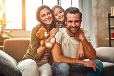 happy-dad-mom-with-their-cute-daughter-teddy-bear-hug-have-fun-sitting-sofa-living-room-home-1.jpg