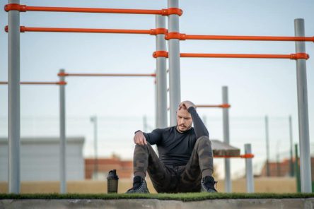 Young Hispanic man sitting on the grass in the sports ground having a rest